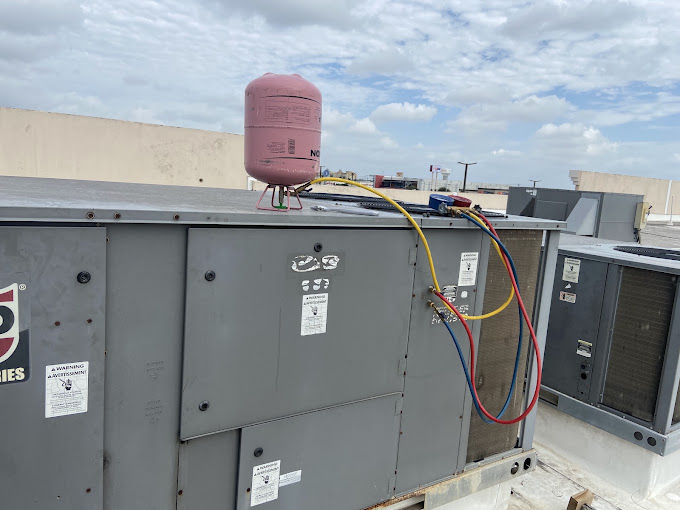 Climate Heating & Cooling technician connecting gauges to service an AC compressor on a rooftop unit in the Rio Grande Valley